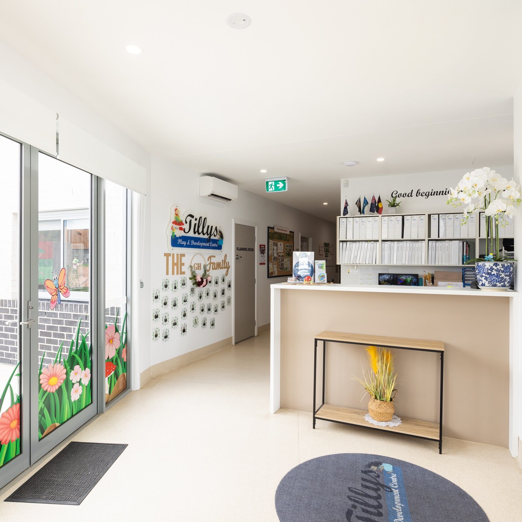 Bright, welcoming reception area with large windows, colorful floral wall art, a sleek desk, and potted plants, creating a cheerful, inviting atmosphere.