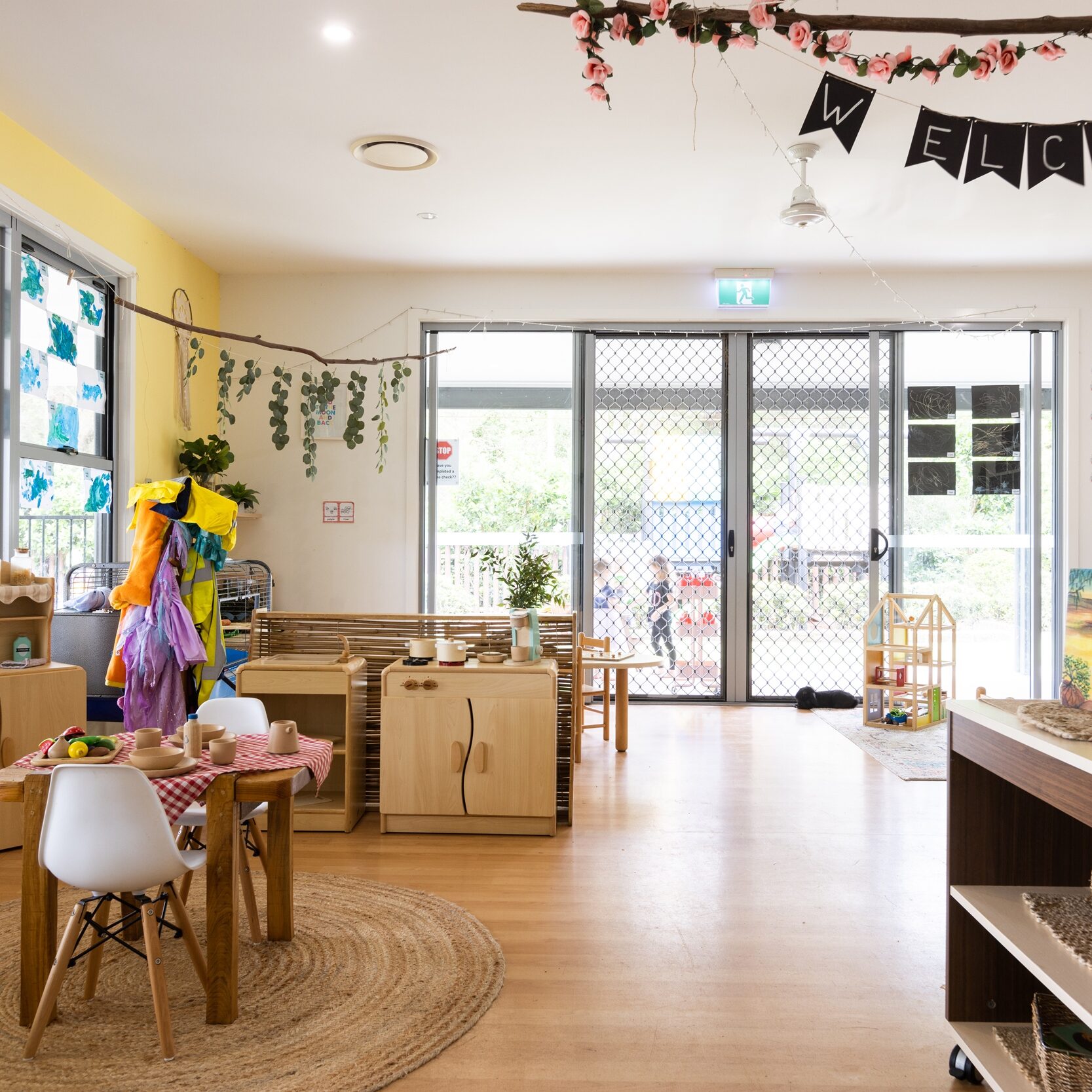 Bright, welcoming preschool classroom with natural light, colorful decorations, play areas, and small tables and chairs; a cheerful and inviting atmosphere.