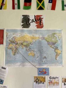 Tillys Rutherford World map with Italy sign above, surrounded by international flags. Below, images of pasta, gelato, and ballet create a cultural theme.
