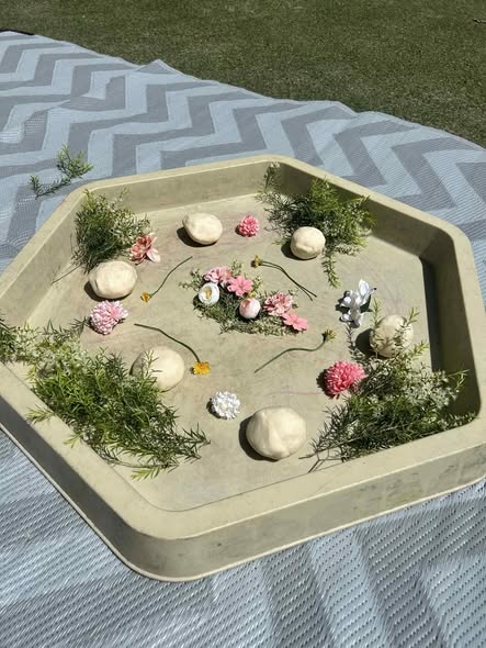 Tillys Waratah 1 Hexagonal tray on patterned mat, holding white play dough balls, pink and white flowers, and greenery. The setup is outdoors, evoking a serene, creative mood.