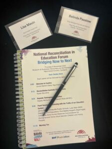 A spiral-bound event program titled “National Reconciliation in Education Forum: Bridging Now to Next” with a pen resting on it. Two name tags, Lisa Mavin and Belinda Passlow, are visible.