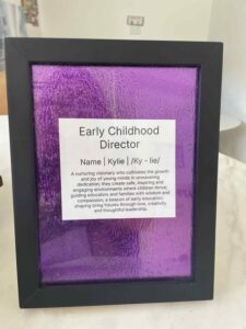 Framed sign with "Early Childhood Director" text, featuring a description of nurturing leadership. Set on a purple textured background, conveying warmth and dedication.