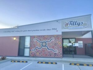Childcare center exterior with a vibrant mural featuring an Aboriginal art design. Sign reads "Educating and caring for your most precious assets since 1994."