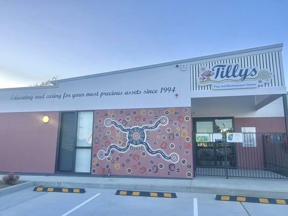 Childcare center exterior with a vibrant mural featuring an Aboriginal art design. Sign reads "Educating and caring for your most precious assets since 1994."