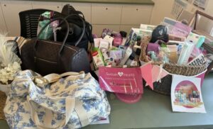 Three large bags and a basket filled with toiletries and supplies are on a table. A pink sign reads "Sustain Health." The scene conveys aid and support.
