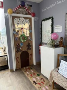 Tillys Rutherford Festively decorated door as a gingerbread house with candy-themed art, wreath, and snowflakes. Warm, inviting classroom setting with playful holiday spirit.