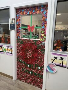 Tillys Rutherford Festive classroom door decorated with colorful Christmas lights and a red bow. Bold green letters spell “Season for Kindness,” creating a joyful, inviting atmosphere.