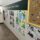 Hallway with children's art displayed on a wall, featuring colorful drawings and paintings. A corkboard with stickers is visible, creating a playful and creative atmosphere.