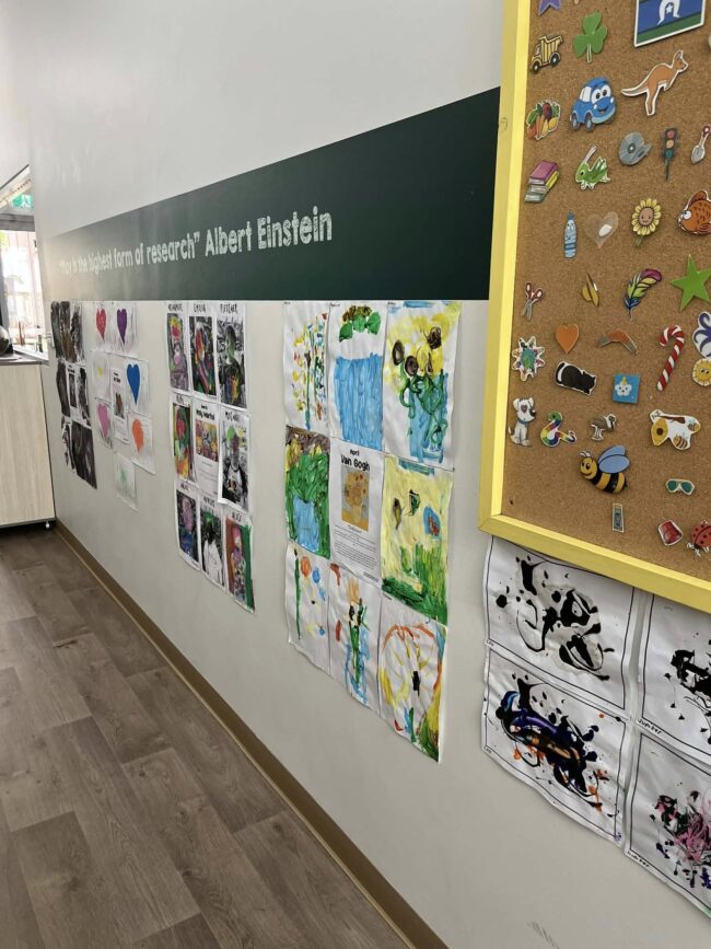 Tillys Rutherford Hallway with children's art displayed on a wall, featuring colorful drawings and paintings. A corkboard with stickers is visible, creating a playful and creative atmosphere.