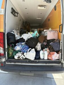 Tillys Cooranbong A van with open back doors filled with a variety of bags and packages, including suitcases, backpacks, and shopping bags. The scene appears cluttered and busy.
