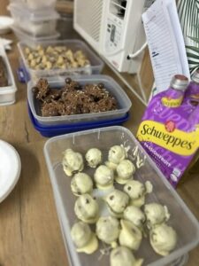 Trays of assorted homemade chocolates, some white-coated, sit on a wooden table. A carton of Schweppes Passionfruit drink is nearby, creating a cheerful scene.
