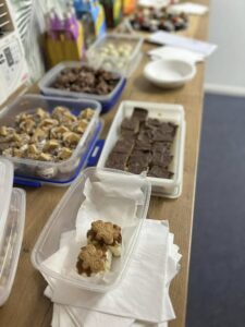A wooden table filled with assorted homemade treats in plastic containers, including chocolate squares and gingerbread, creating a cozy, inviting atmosphere.