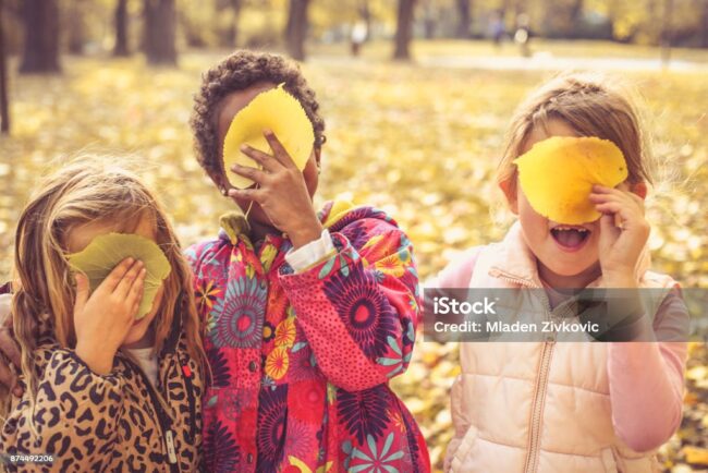 Three little girls playing with fallen leaves.